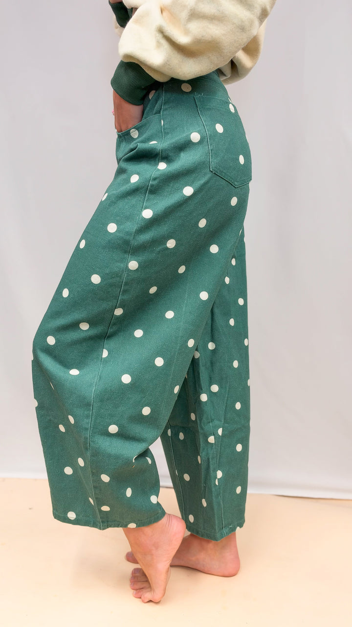 Woman shown from side view wearing green polka dot barrel jeans on plain background