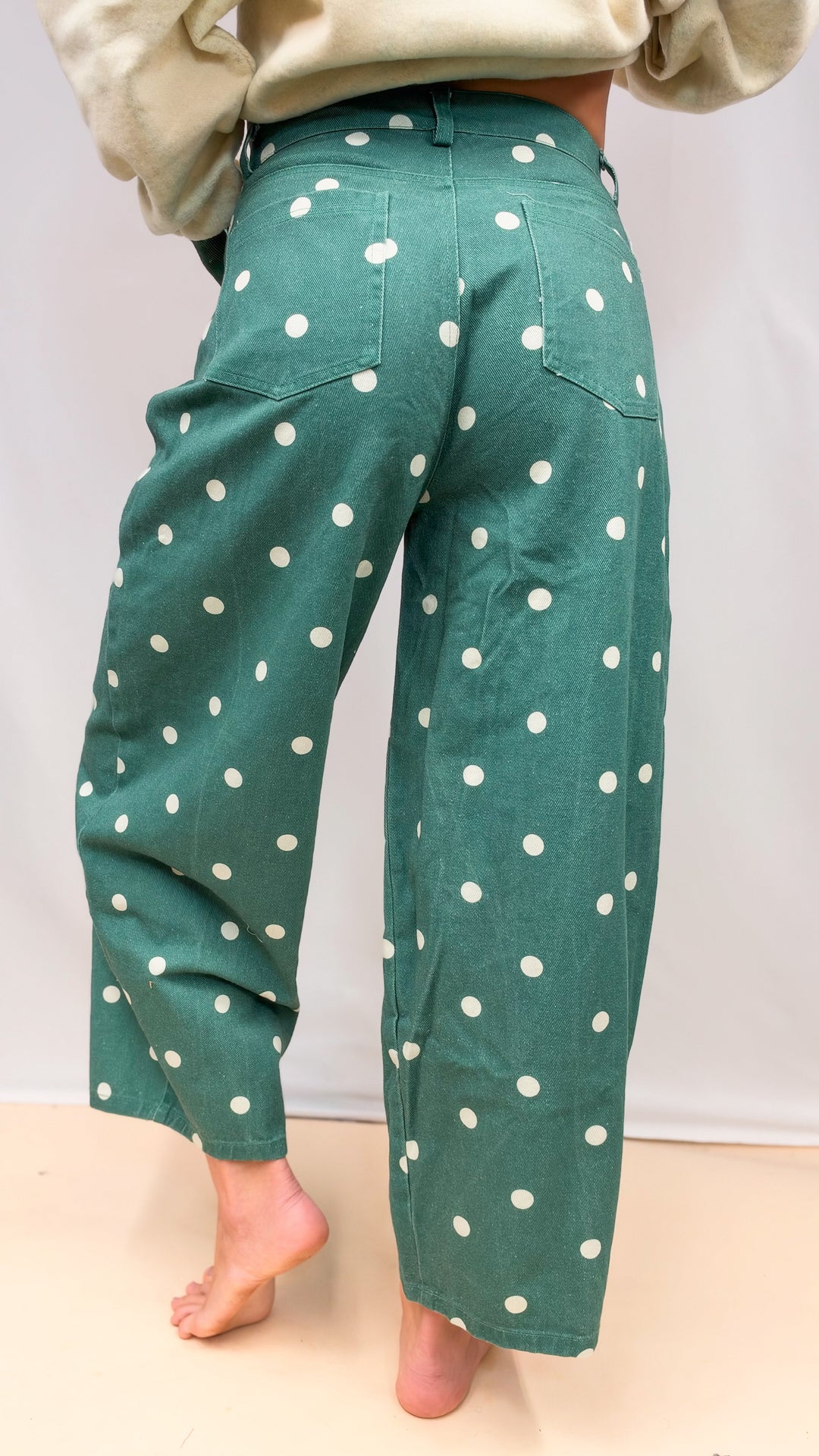 Woman shown from back view wearing green polka dot barrel jeans on plain background