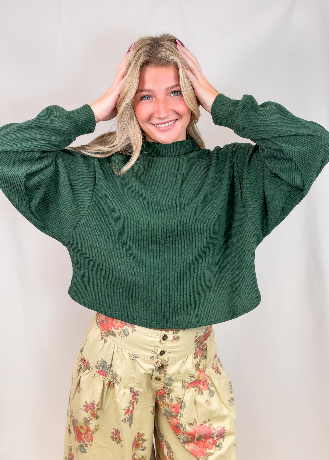 Woman wearing green mock neck sweater with floral pants on plain background