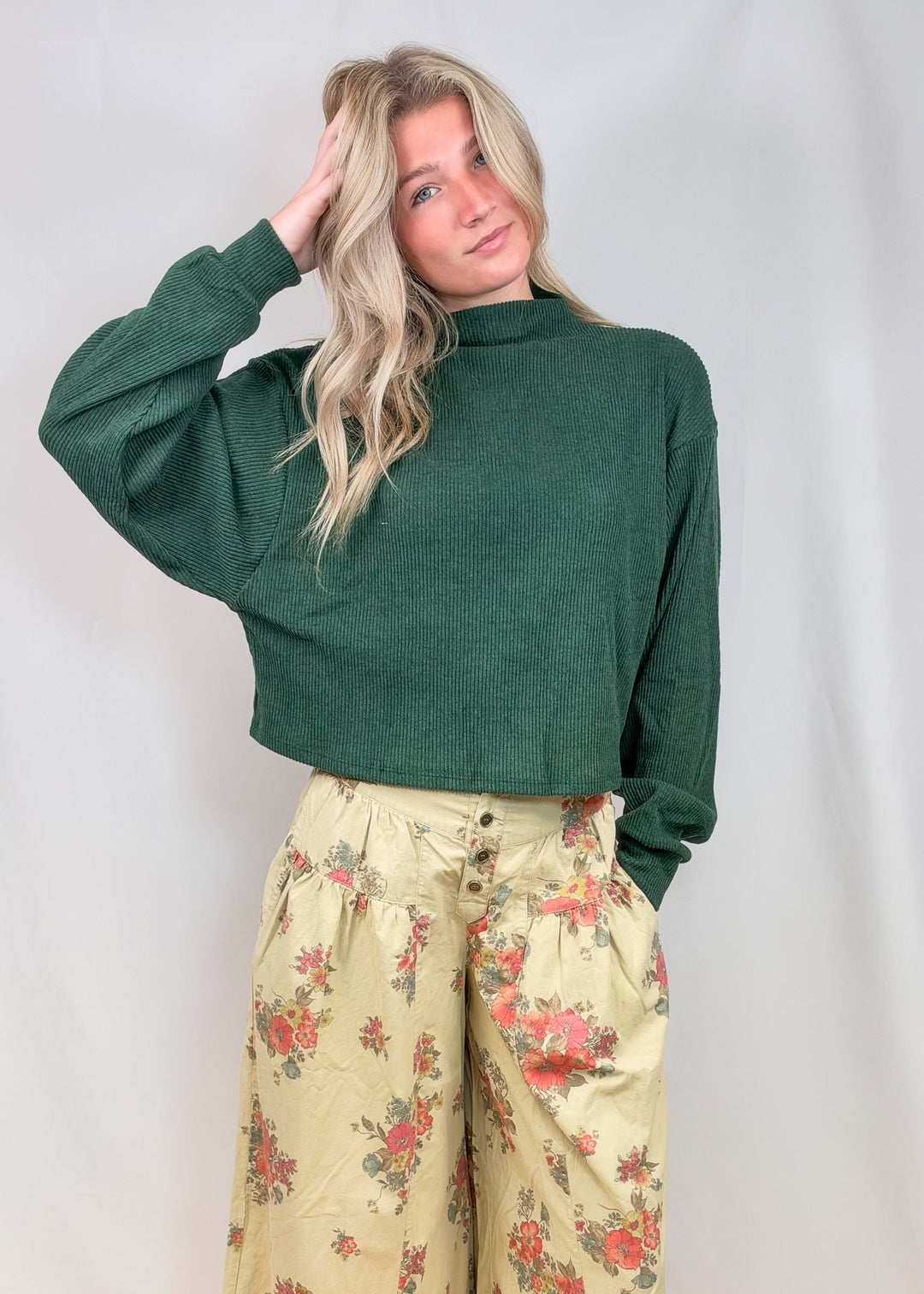 Woman wearing green mock neck sweater with floral pants on plain background