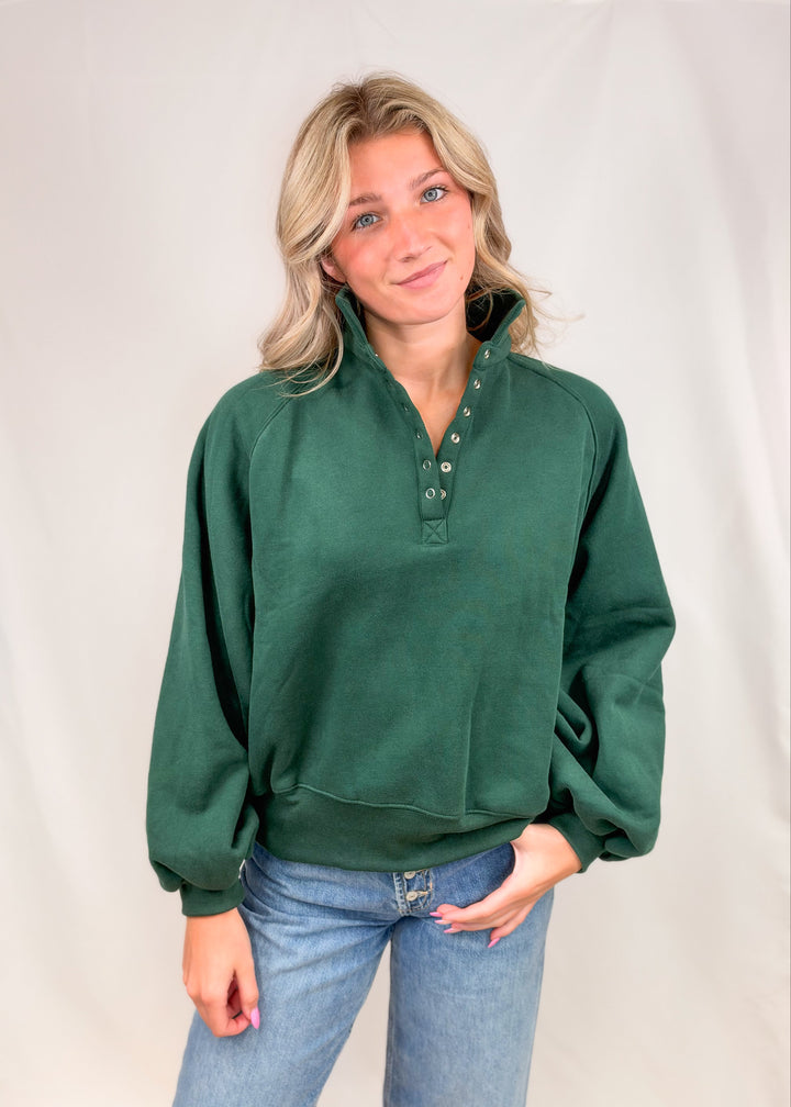 Woman wearing green snap collar sweatshirt with jeans on plain background