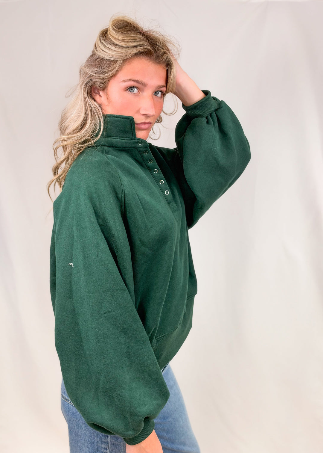 Woman wearing green snap collar sweatshirt with jeans on plain background