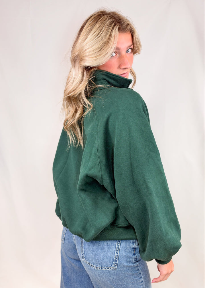Woman shown from back wearing green sweatshirt and jeans on plain background