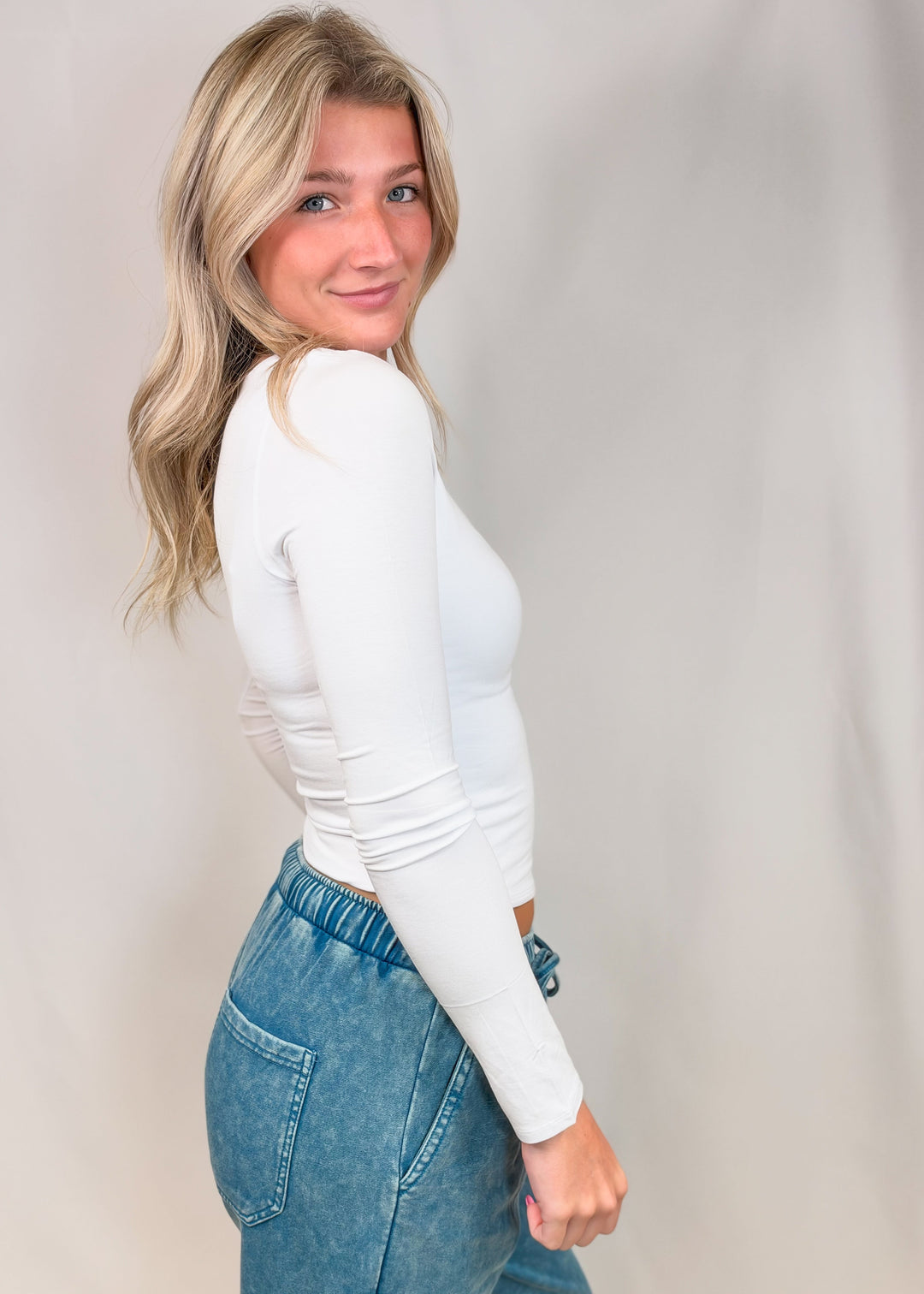 Woman wearing white long sleeve top on plain background