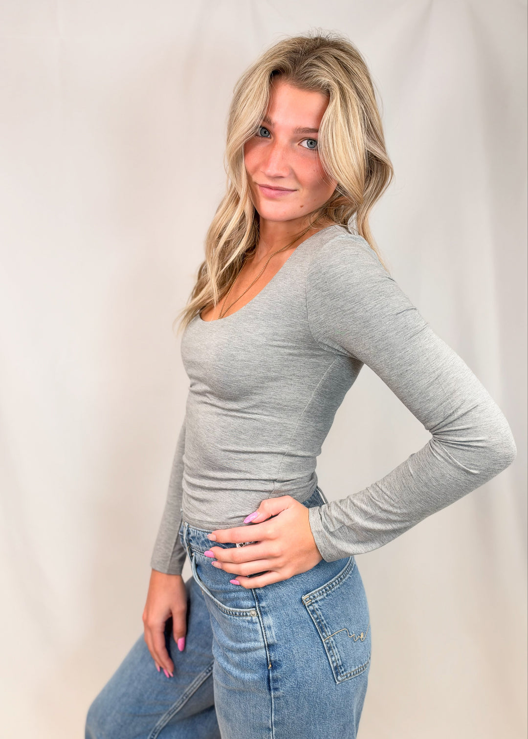 Woman wearing grey long sleeve top on plain background