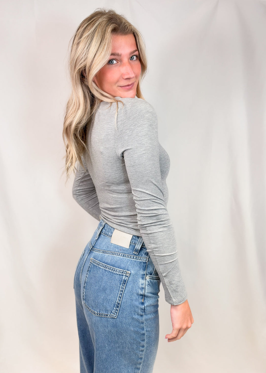 Woman shown from back wearing grey long sleeve top on plain background