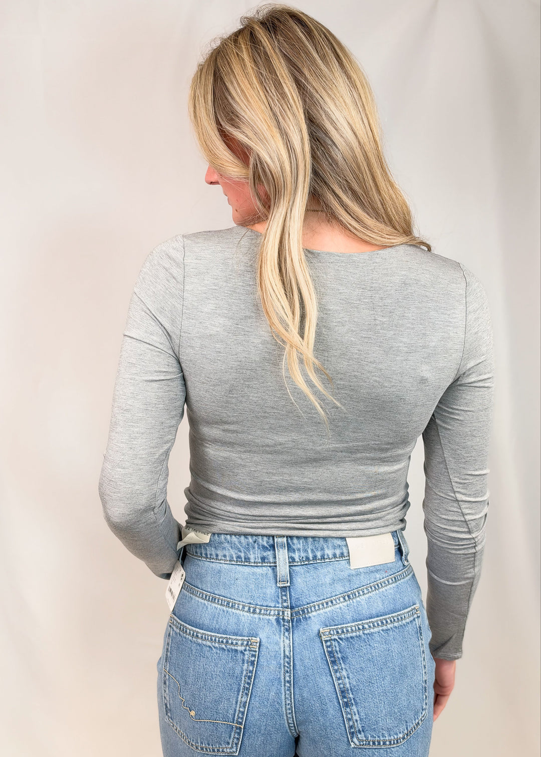 Woman shown from back wearing grey long sleeve top on plain background