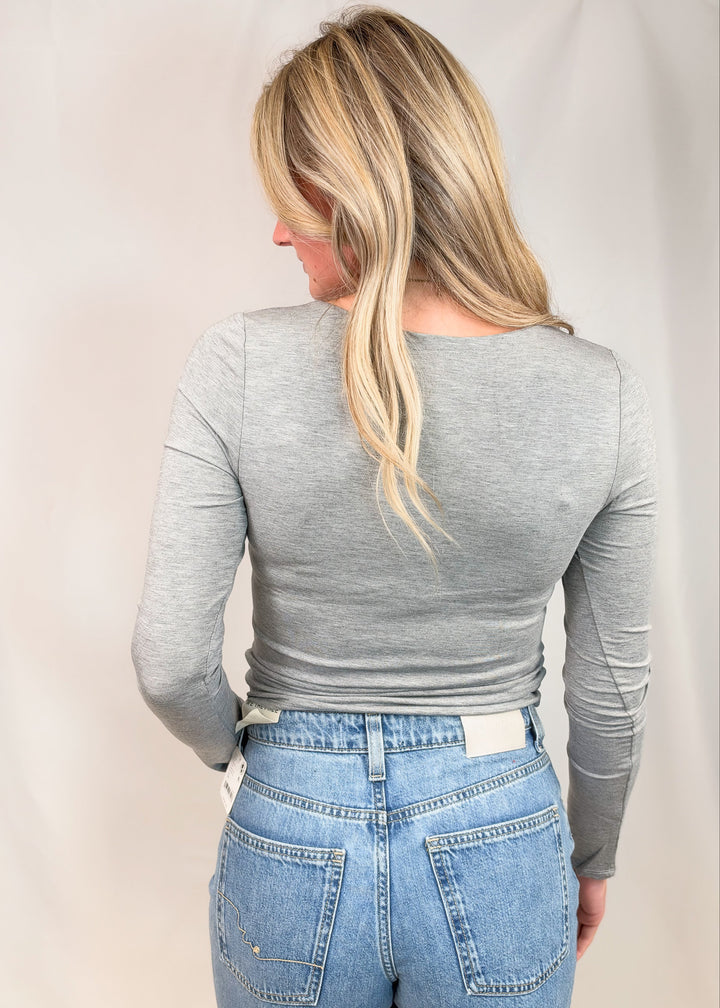 Woman shown from back wearing grey long sleeve top on plain background