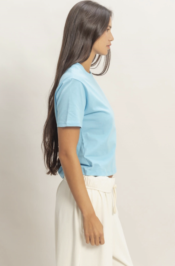 Woman wearing a light blue t-shirt and white pants against a plain background