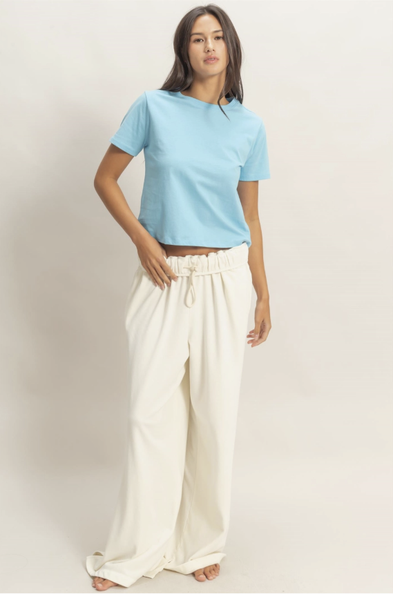 Woman wearing a light blue top and white pants on a plain background