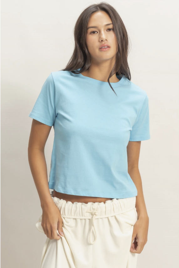 Woman wearing a light blue t-shirt and white pants against a neutral background