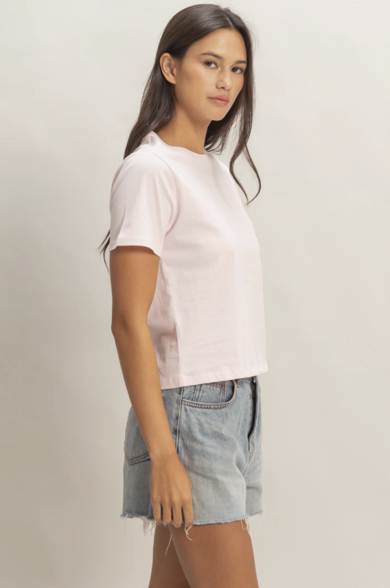 Woman wearing a light pink t-shirt and denim shorts on a plain background