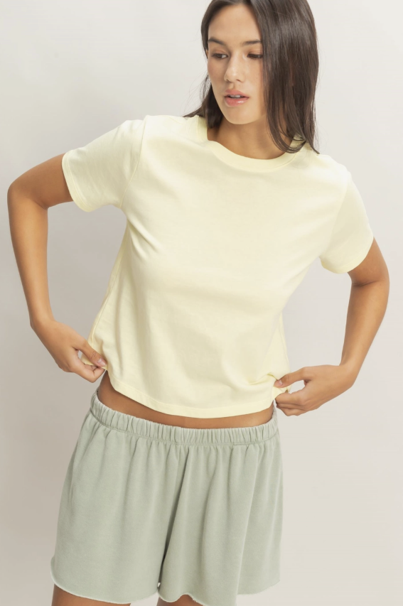 Woman wearing a light yellow t-shirt and light green shorts on a plain background