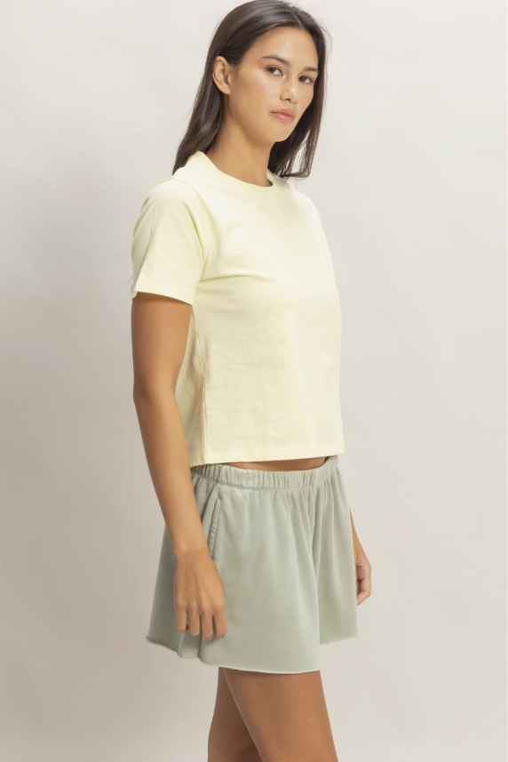Woman wearing a light yellow top and green skirt on a plain background