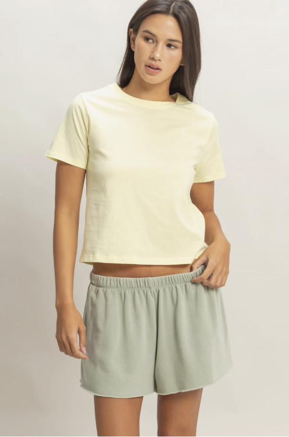 Woman wearing a light yellow crop top and light green shorts on a plain background