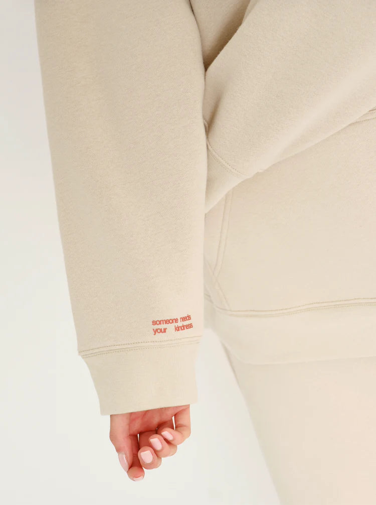 Beige hoodie with red text on sleeve against a white background