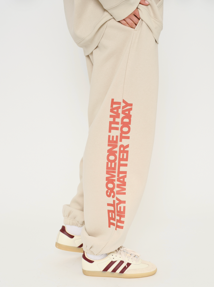 Beige sweatpants with red text and beige sneakers on a white background