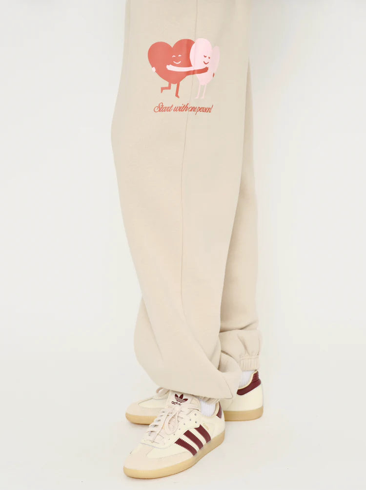 Beige sweatpants with a heart design and text on a white background