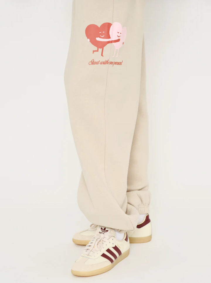 Beige sweatpants with a heart design and text on a white background