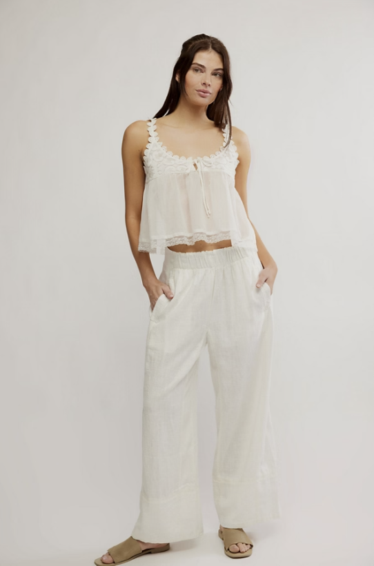 Woman wearing a white sleeveless top and wide-leg pants on a plain background