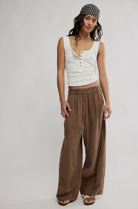 Woman wearing a white tank top and brown wide-leg pants on a plain background