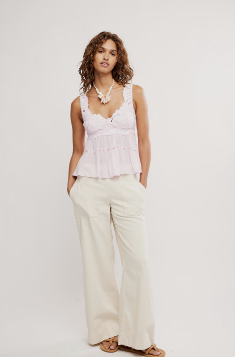 Woman wearing a light pink sleeveless top and white pants on a plain background