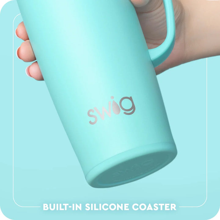 A hand holding a light blue insulated tumbler with the Swig logo, showing a built-in silicone coaster at the bottom. The background is a matching light blue with a white border and text reading &