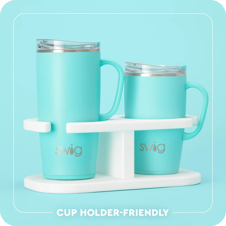 Two mint green Swig insulated tumblers with clear lids and handles, displayed on a white cup holder stand against a light blue background. White text at the bottom reads &