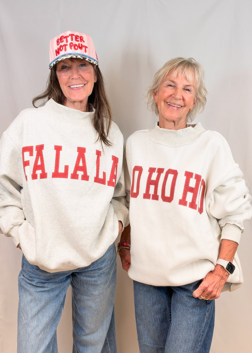 Two women wearing grey mock neck with 'FA LA LA' and 'HO HO HO' on plain background
