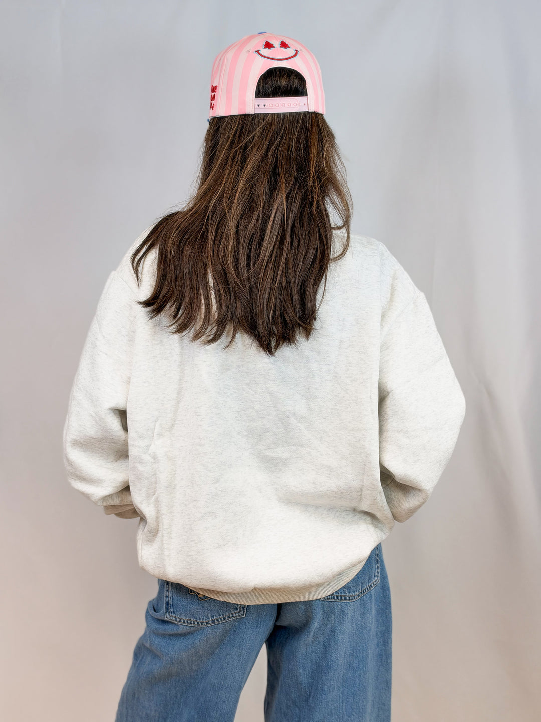 Woman shown from back wearing grey mock neck sweatshirt and jeans on plain background