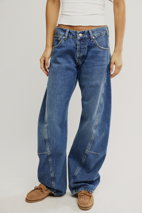 Person wearing blue jeans and brown shoes on a plain background