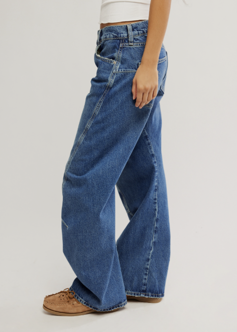 A person wearing wide-leg blue denim jeans with a white cropped top and brown lace-up shoes, shown from the waist down against a plain light gray studio background.