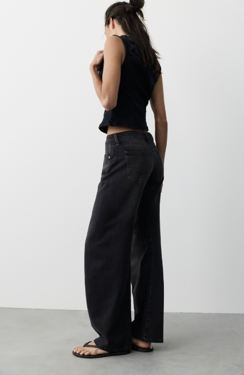 Woman wearing black tank and black jeans on plain background