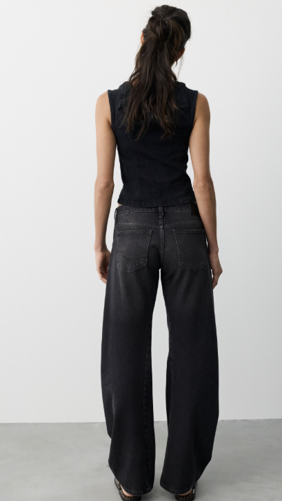 Woman shown from behind wearing black tank and black jeans on plain background