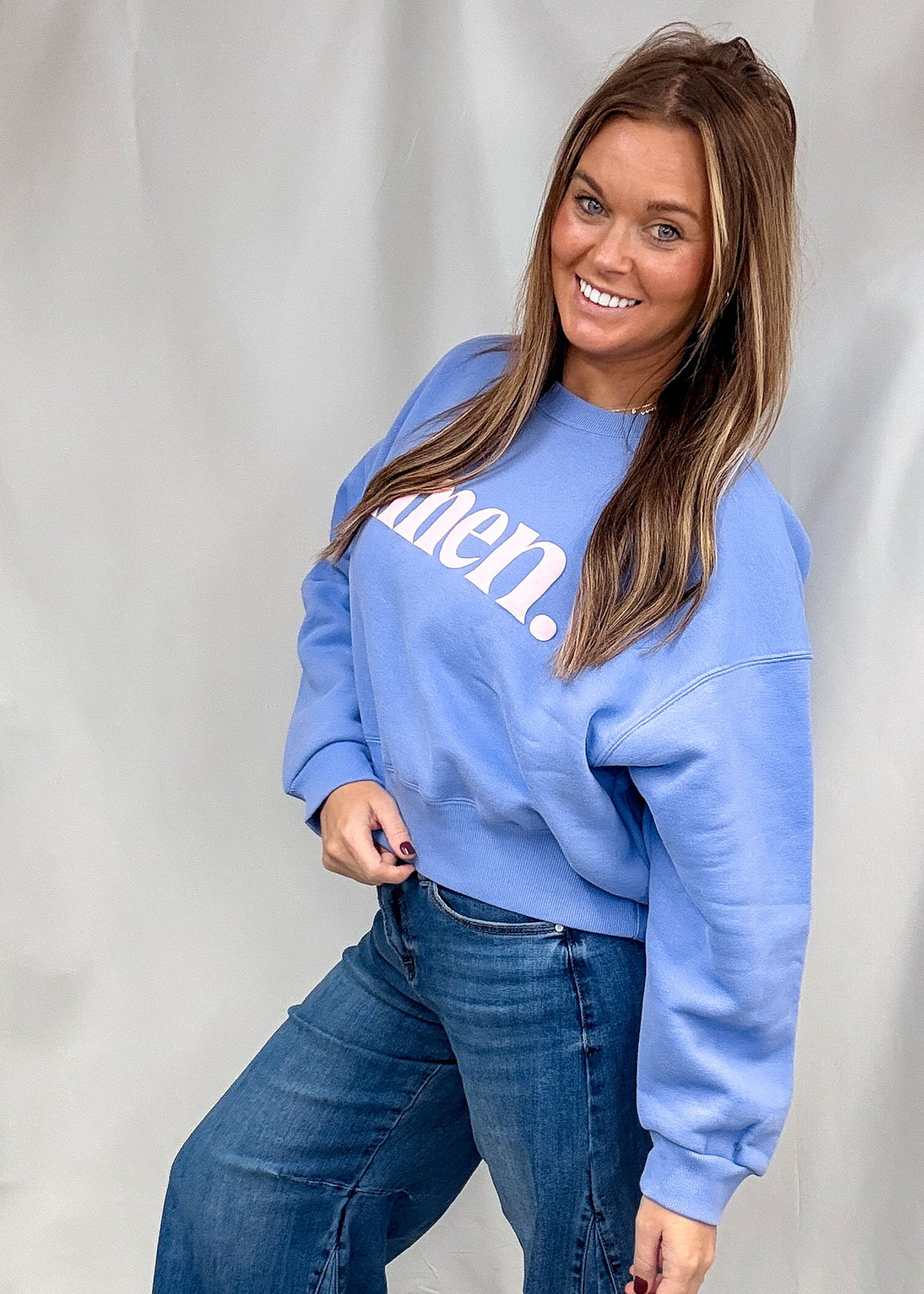 A woman modeling a light blue crewneck sweatshirt with white text that reads &