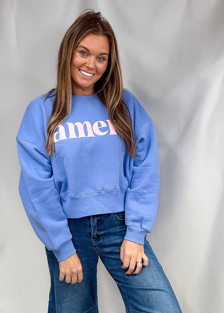 A woman wearing a light blue crewneck sweatshirt with &