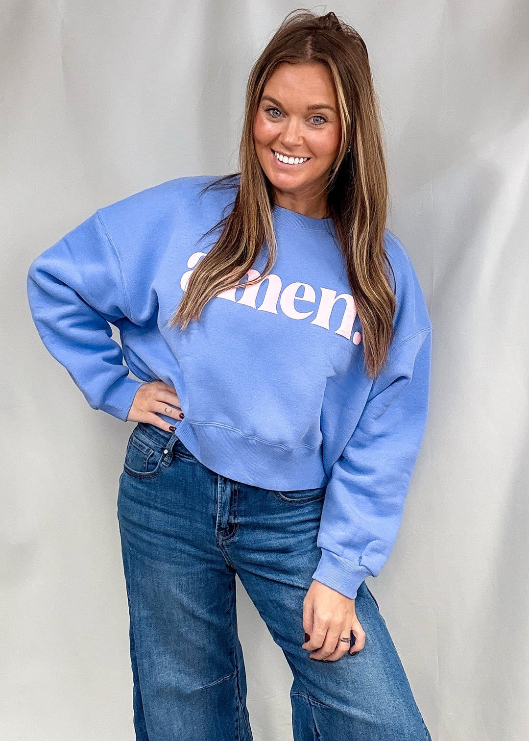 A woman modeling a light blue crewneck sweatshirt with white text that reads &