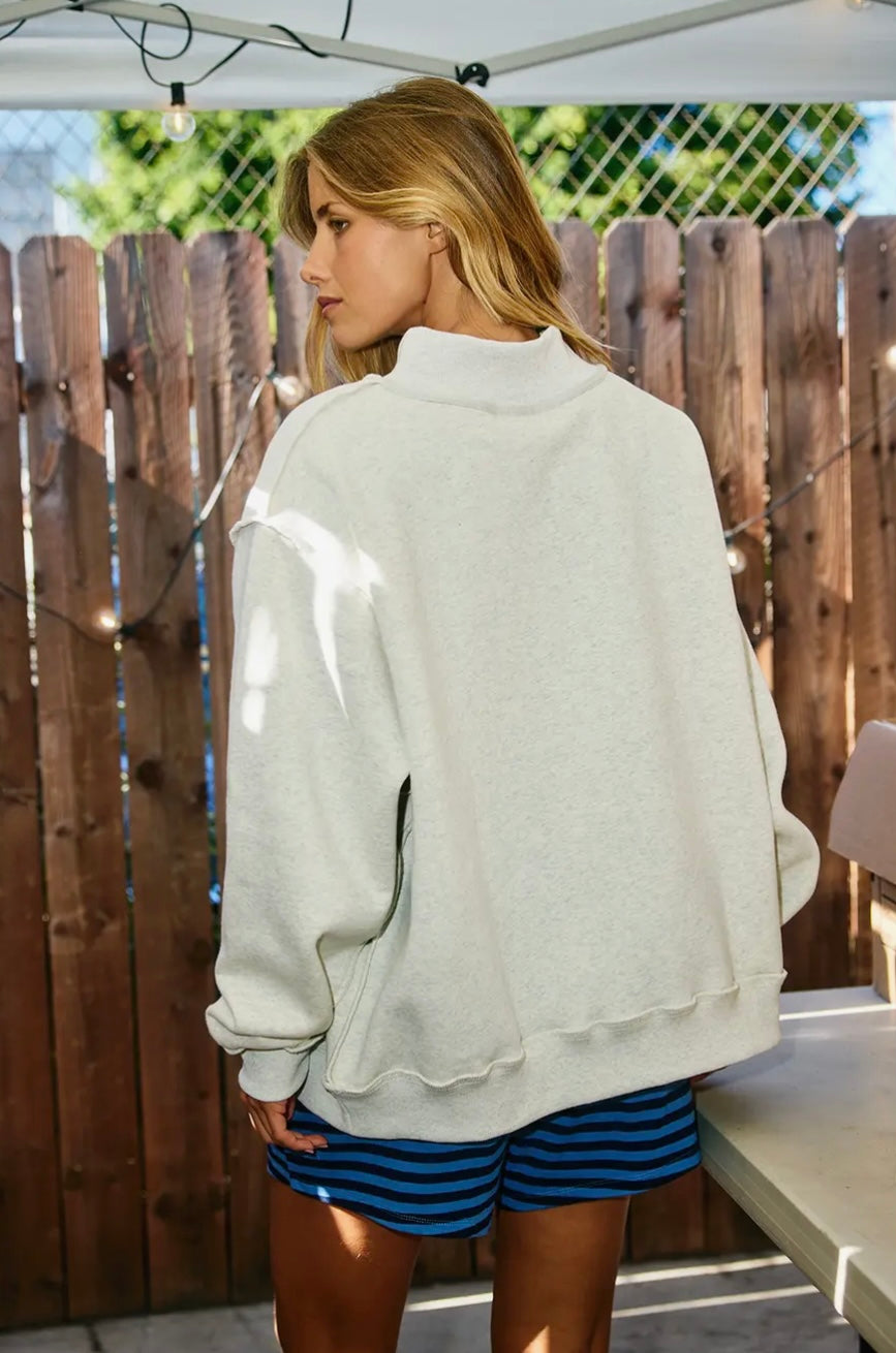 Woman wearing a light gray sweatshirt and blue shorts standing outdoors with a wooden fence in the background.