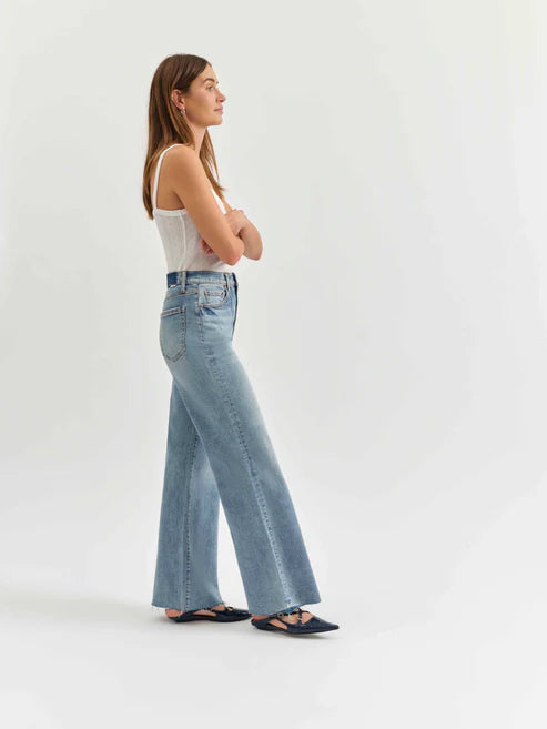 Woman wearing light blue flared jeans and a white top on a white background