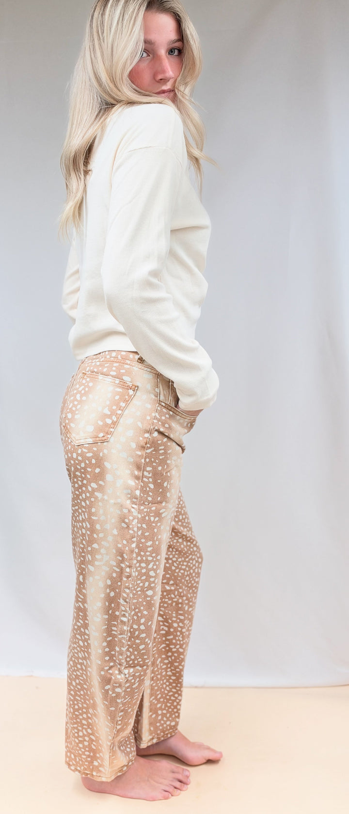 Woman shown from side view wearing beige color top with fawn print denim barrel jeans on plain background