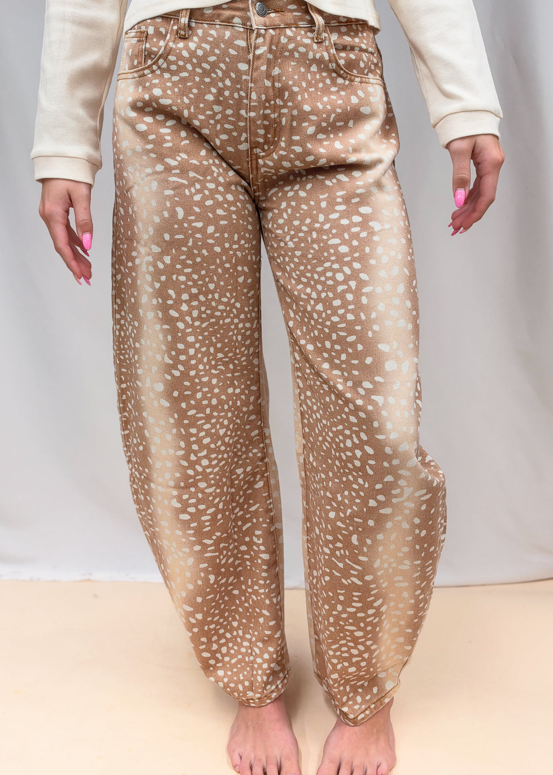 Woman wearing beige color top with fawn print denim barrel jeans on plain background