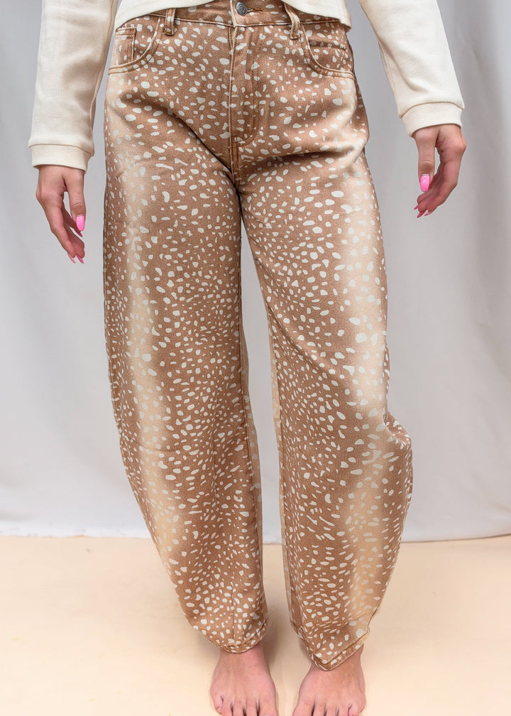 Woman wearing beige color top with fawn print denim barrel jeans on plain background