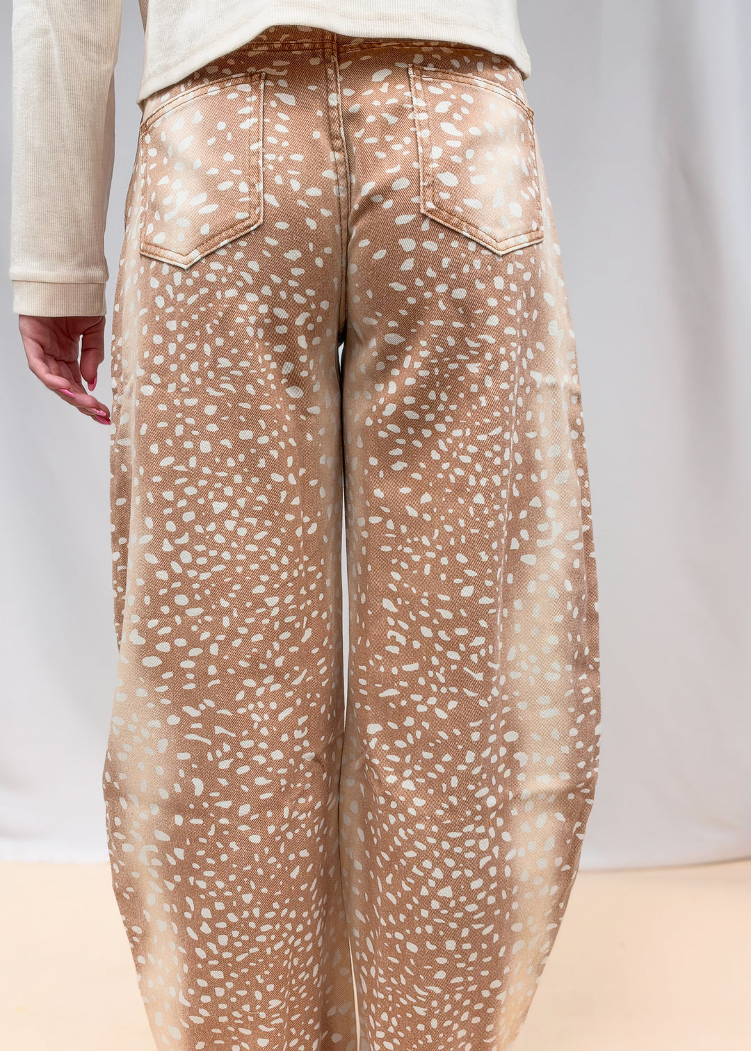 Woman shown from back view wearing beige color top with fawn print denim barrel jeans on plain background