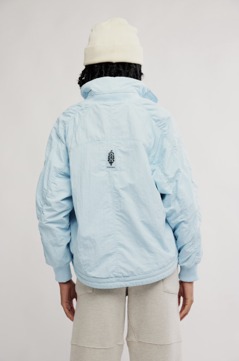 Person wearing a light blue quilted jacket with a logo on the back against a plain background