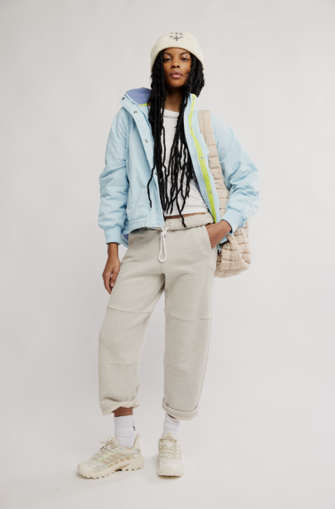 Person wearing a light blue jacket, beige pants, and white sneakers on a plain background