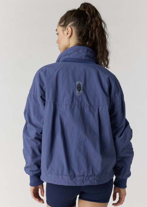 Woman shown from back wearing navy pullover jacket and navy bike shorts on plain background