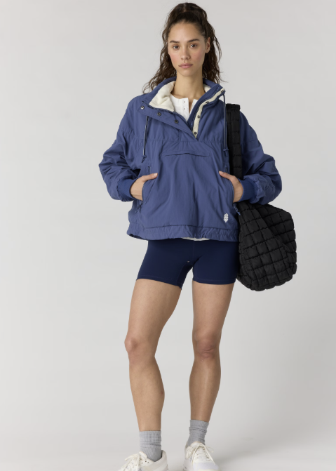 Woman wearing navy pullover jacket with navy bike shorts on plain background
