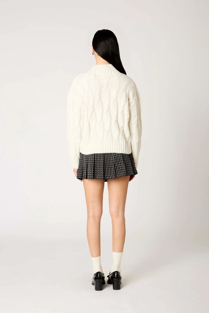 Person wearing a white cable knit sweater and plaid skirt on a white background
