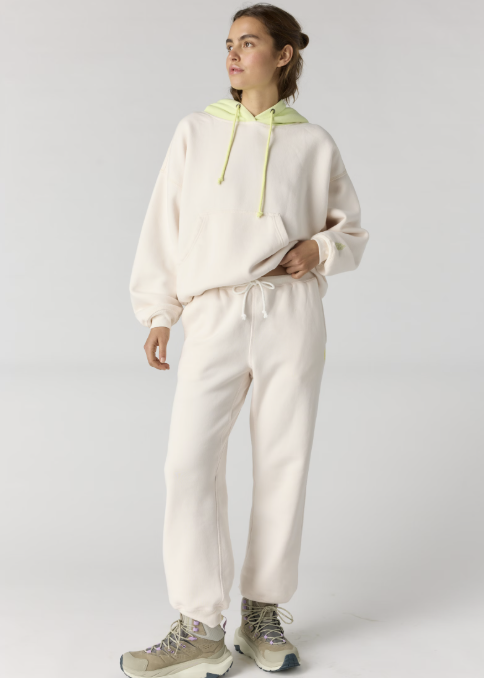 Woman wearing matching cream sweatshirt and sweatpants with yellow accents on plain background