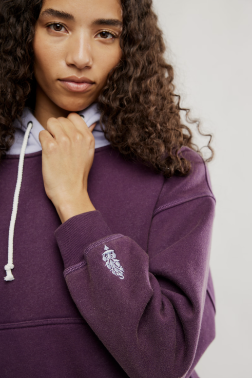 Person wearing a purple hoodie with a logo on a plain background